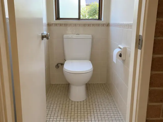 Clean white toilet in a tiled bathroom with a window and tiled floor in Caringbah